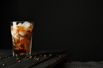 Wall Mural - Pouring cream into a glass with iced coffee on table and black background