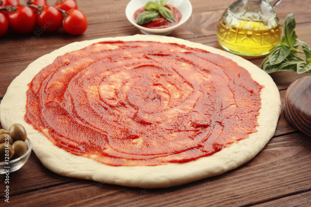 Raw pizza dough with sauce and ingredients on wooden table
