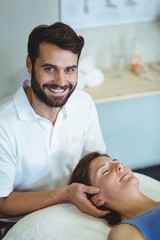 Wall Mural - Smiling physiotherapist giving head massage to a woman