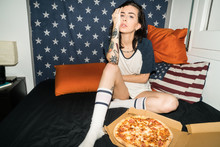 Young Woman Sitting On Bed With Pizza