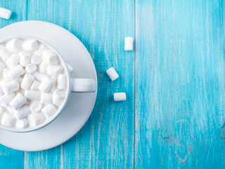 Wall Mural - A cup of hot cocoa with marshmallows and sticks of cinnamon on a bright blue wooden background shabby. Shallow Selective focus. Copyspace. Top view.