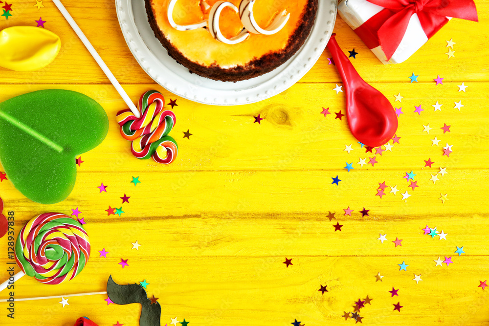 Birthday party objects on yellow wooden background, top view