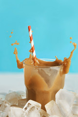 Wall Mural - Glass of cold coffee with ice cubes and splashes on table