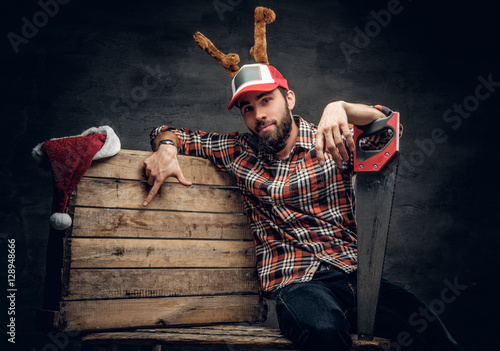 Foto-Kissen - A bearded male in Christmas cap with deer horns holds handsaw. (von Fxquadro)