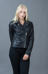 Portrait of a blond girl in a leather jacket gray studio backgro