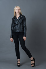 Portrait of a blond girl in a leather jacket gray studio backgro