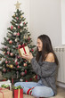 © nikodash - Beautiful woman sitting next to Christmas tree opening presents