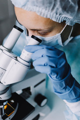 Wall Mural - from above view of young scientist in work uniform looking at microscope.