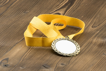 Gold medal with white placeholder and yellow ribbon on wooden textured table