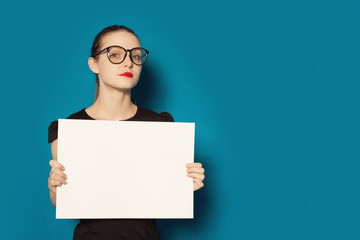 Pretty young woman showing on empty blank board. Colorful studio portrait isolated on blue background. Space for text.