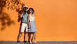 Happy smiling couple near orange sunny wall outdoor. Summer vacation, enjoy holiday