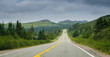 Newfoundland highway in overcast skies.  Lone car goes down the road.  Coastal highways in foothills and valley ranges of Newfoundland. 