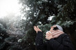 © iuricazac - Beautiful young caucasian woman in winter jacket, knitted beanie gray hat and pink scarf, holding a cup of coffee or tea, outdoors in park or forest on snowing winter day. Winter mood.