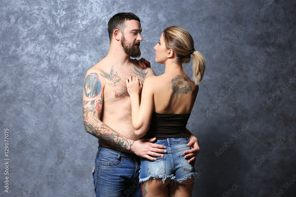 Passion tattooed beautiful couple on gray wall background