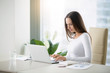 © fizkes - Young woman working at the modern office desk with a laptop, busy with distance learning, tutoring, making online surveys. Lady boss at her workplace. Business success concept