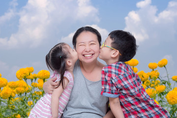 Wall Mural - Asian boy and girl kissing their mother in park