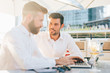 © Eugenio Marongiu - Two young contemporary businessmen working outdoor sitting in a bar using a smart phone and a notebook, both smiling - technology, business, work concept - copy space on left