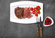 Sliced tasty steak with spices and tomatoes on white plate