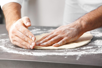 Male hands preparing dough for pizza on table closeup