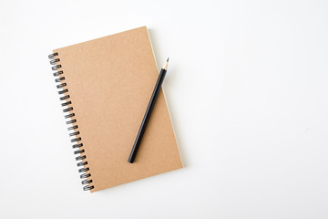 top view of closed spiral blank craft paper cover notebook with pencil on white desk background