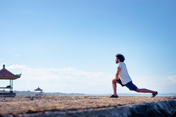 Sports lifestyle. Happy young african man stretching on the sea shore.