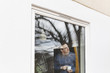 © Maskot - Man holding coffee cup looking through window while standing in house