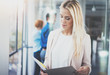 © SFIO CRACHO - Portrait of young pretty blonde businesswoman in modern coworking studio with business team on the background.Beautiful woman near the window holding papers in hands.Horizontal,blurred.