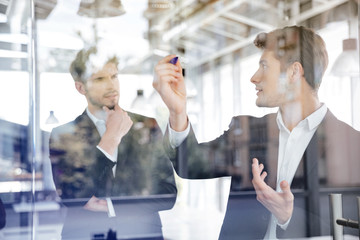 Poster - Two businessmen talking and writing on glass board in office