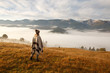 © Serhii - young woman hiking at mountain peak above clouds and fog Hiker girl wrapping in warm poncho outdoor.Early morning.Misty mountain.Young girl over the clouds in the valley looking at calm autumn sunrise