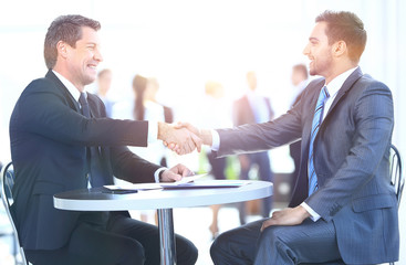 Business colleagues sitting at a table during a meeting with two male executives shaking hands