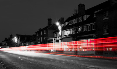 Traffic passing through a village in a monochrome filter with single red and white light trails