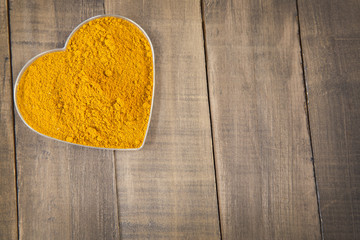 Turmeric spice in a bowl in the form of heart on a wooden background