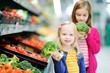 © MNStudio - Two cute little sisters choosing broccoli in a food store or a supermarket