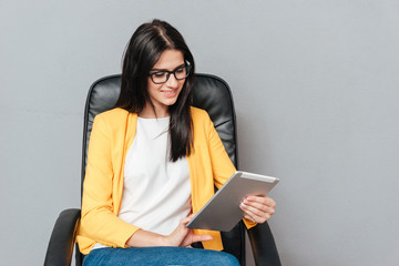 Wall Mural - Cheerful woman sitting on office chair while using tablet computer