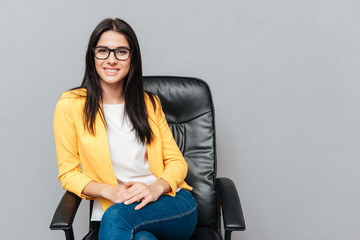 Wall Mural - Cheerful young woman sitting on office chair over grey background.