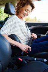 Wall Mural - Smiling woman with curly hair buckling seat belt in car