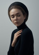 Dramatic portrait of a young beautiful girl with freckles in a black turtleneck and a hat on her head on a white background in studio