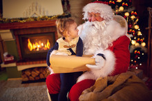 Sweet Girl And Santa Claus Choosing Her Present From List.
