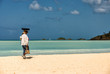 Beach vendor walks along tropical beach with green ocean background