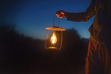 man holding the old lamp with a candle outdoors. hand holds a large lamp in the dark. ancient lanter
