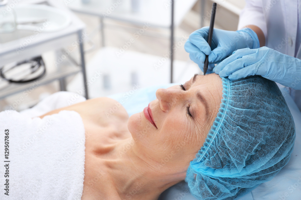 Surgeon hand drawing marks on female face for plastic operation