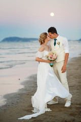 Wall Mural - Moon raises over gorgeous wedding couple kissing on sea shore