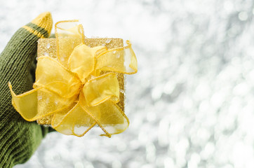 Hand in gloves holding gold christmas gift box on light backgrou