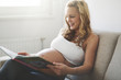 © NDABCREATIVITY - Pregnant woman reading book on sofa