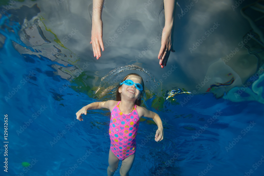 Beautiful little girl swims underwater in the pool to the hands of her ...
