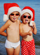 © Evgeniy Kalinovskiy - children on the beach in santa hat and sunglasses on the background sea grimace. Winter holidays in warm countries