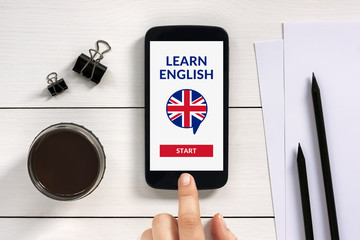 Wall Mural - online learn english concept on smart phone screen with office objects on white wooden table. all sc