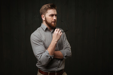 Wall Mural - Pensive bearded man in shirt holding eyeglasses and looking away