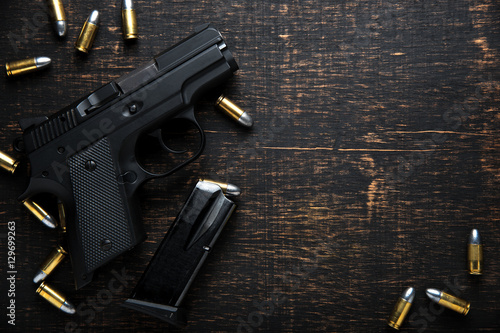Cuadros en Lienzo Gun and ammunition on dark wooden table. top view