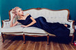 Beautiful blond woman lying on sofa in black dress.